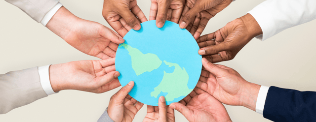 circle of hands holding a paper cutout of the globe