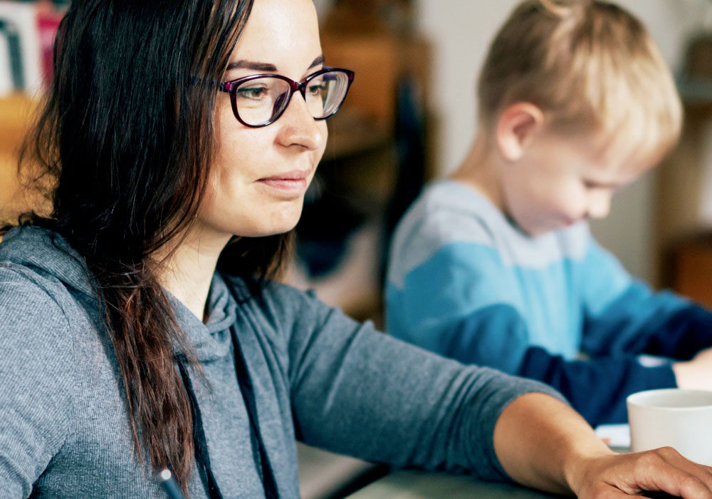 Home worker using a laptop while her child plays alongside